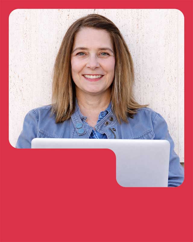 Kim with dark blond hair smiling at the camera behind her laptop.